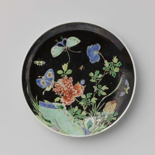 Saucer with butterflies and flowering plant near a rock by anonymous